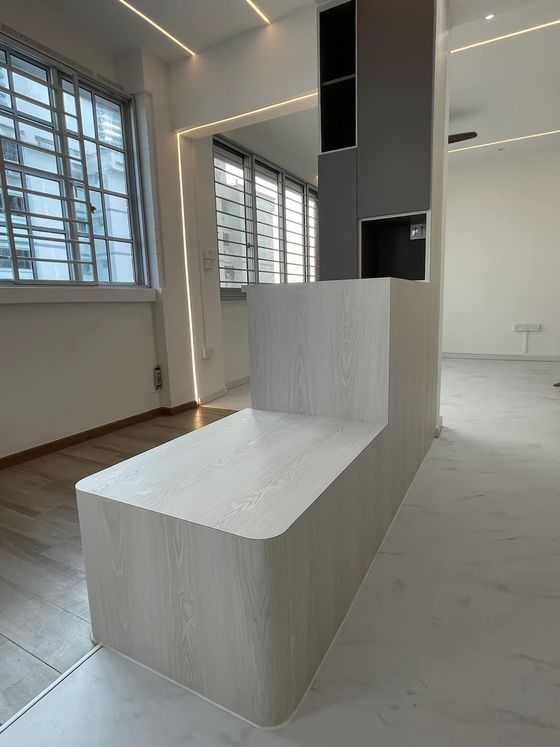Pale wood-grain L-shaped bench and half-height partition with a rounded return, backed by a charcoal display column.