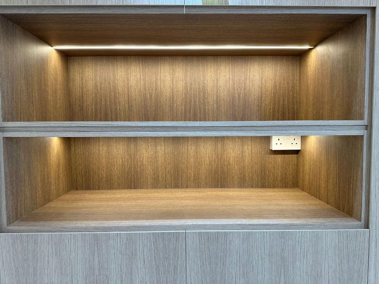 Close detail of a pale wood-grain open shelving unit with concealed LED strips above and below the shelf.