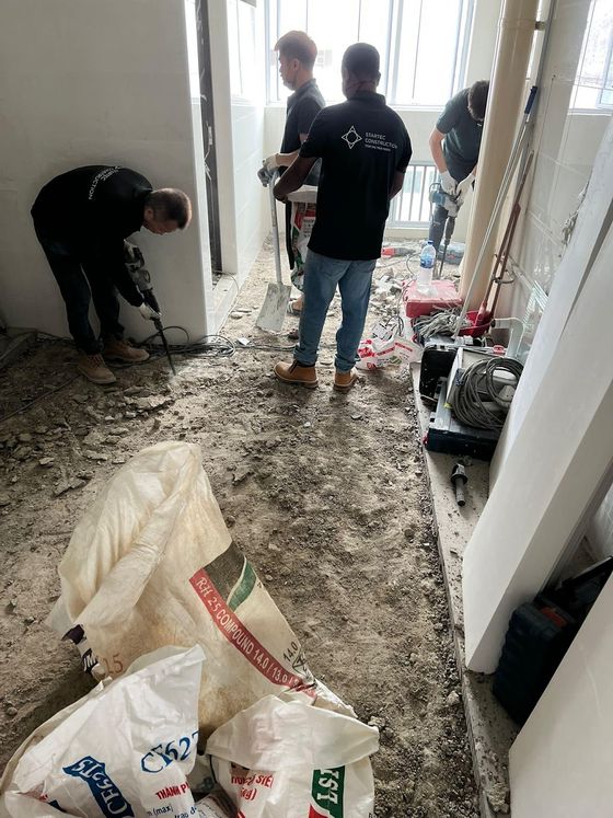 Three Startec crew in black company polos hacking out an existing wall and floor, with rubble sacks in the foreground.