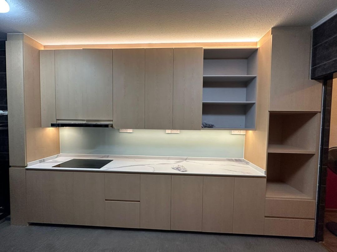 Pale wood-grain handleless kitchen with a marble-pattern worktop, open shelving and LED cove lighting, built by Startec.