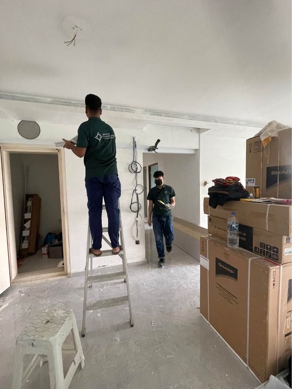 Two Startec team members in company polo shirts working inside a flat mid-renovation, one on a ladder finishing the ceiling.